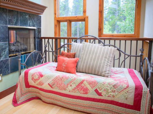 Cozy seating area with a quilted bedspread, decorative pillows, and a fireplace, surrounded by large windows.