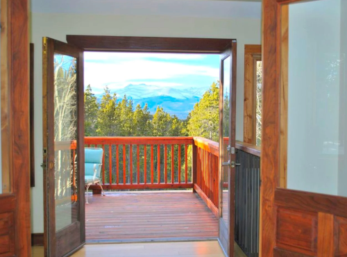 A scenic view from an open doorway, showcasing a wooden deck and mountains in the background.