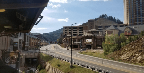 A view of a mountain town with a casino, empty roads, and buildings under a blue sky with scattered clouds.