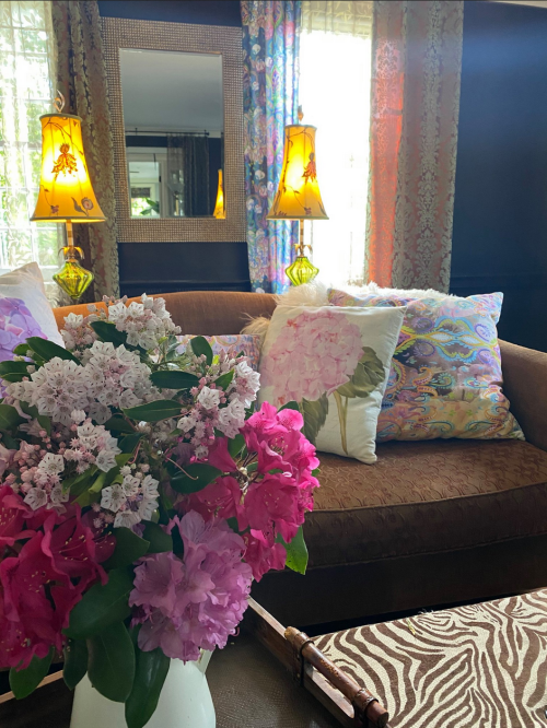Cozy living room with a brown sofa, colorful pillows, a floral arrangement, and warm lamp lighting.