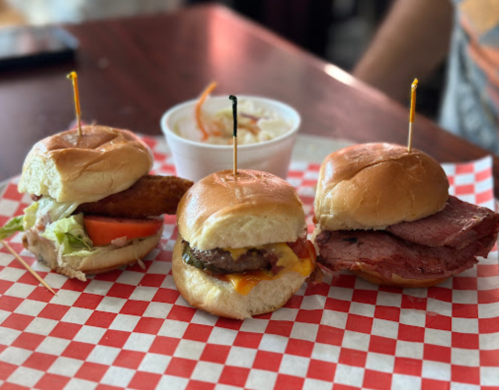 Three mini sandwiches on a red and white checkered plate: a chicken sandwich, a cheeseburger, and a roast beef sandwich.