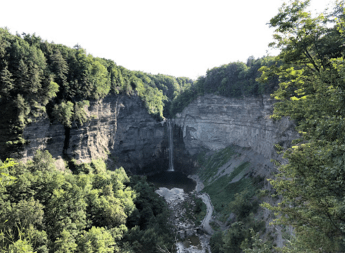 A scenic view of a waterfall cascading into a lush, green gorge surrounded by steep cliffs and trees.