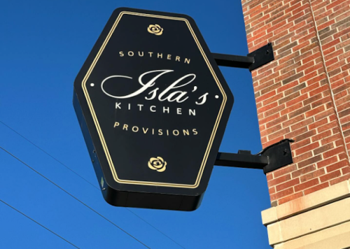 Sign for Isla's Kitchen, a Southern provisions restaurant, featuring a black hexagonal design against a blue sky.