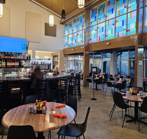 Interior of a modern restaurant featuring a bar, colorful stained glass windows, and tables set for dining.