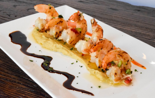 Grilled shrimp on a bed of creamy sauce, drizzled with balsamic glaze and garnished with herbs.