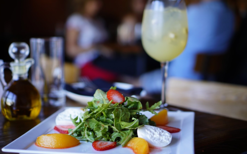 A fresh salad with arugula, strawberries, and peaches, served with a drink in a restaurant setting.