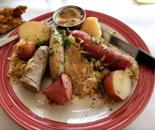 A plate of assorted sausages, sauerkraut, and red potatoes, garnished with parsley and served with mustard.