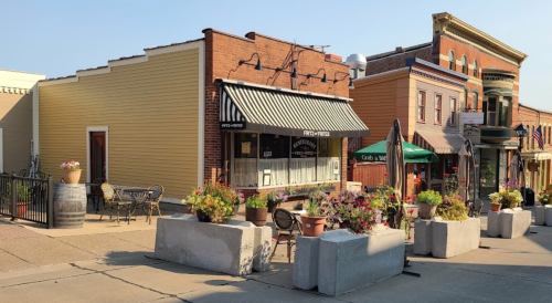 Charming street scene featuring a café with outdoor seating and colorful flower pots in a quaint town.