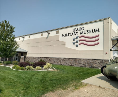 Exterior of the Idaho Military Museum featuring a large sign and American flag design, surrounded by greenery.