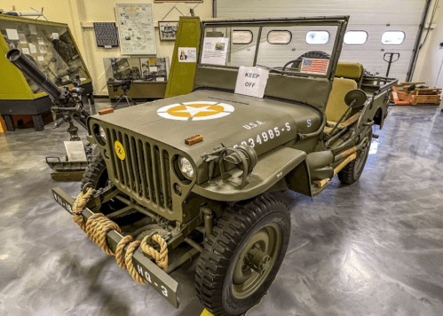 A vintage military jeep displayed in a museum, featuring a star insignia and a "Keep Off" sign.