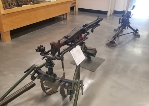 Two mounted machine guns displayed in a museum setting, with informational tags nearby.