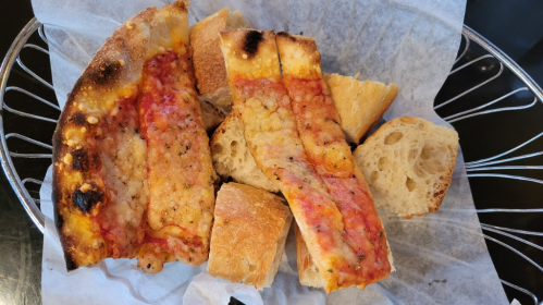 A plate of toasted bread with crispy edges, topped with tomato sauce and cheese, alongside pieces of crusty bread.