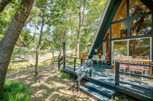 A modern A-frame cabin surrounded by trees, featuring a deck and large windows overlooking a serene outdoor area.
