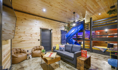 Cozy room with wooden walls, a blue slide, bunk beds, bean bags, and a sofa, creating a playful atmosphere.