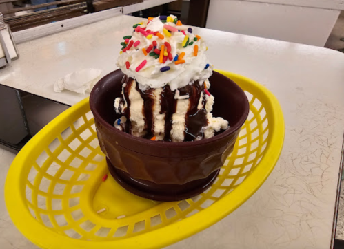 A large ice cream sundae topped with whipped cream, chocolate sauce, and colorful sprinkles in a brown bowl.