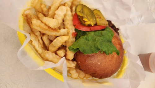 A plate with a burger topped with lettuce, tomato, and pickles, alongside a serving of crinkle-cut fries.