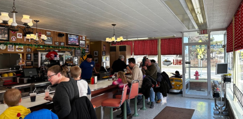 A busy diner interior with patrons at the counter, families seated, and a bright, welcoming atmosphere.