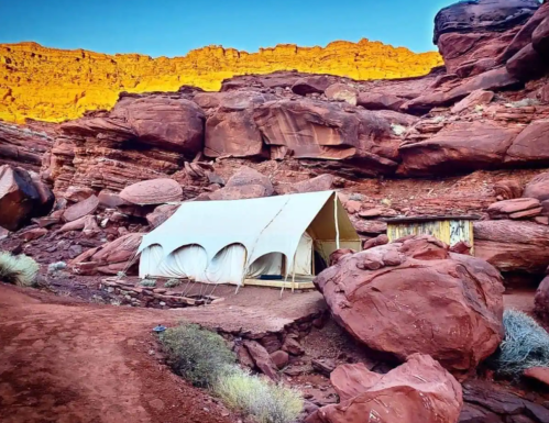 A large white tent set against red rock formations and a clear blue sky in a desert landscape.