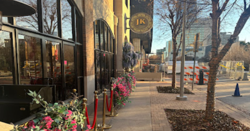 Exterior view of a restaurant with floral decorations, red ropes, and construction barriers in the background.