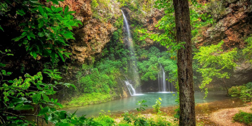 A serene waterfall cascades into a tranquil pool, surrounded by lush greenery and rocky cliffs.