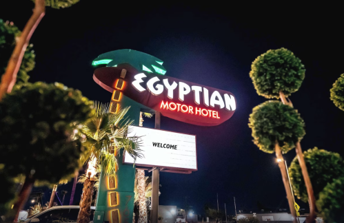 Neon sign for the Egyptian Motor Hotel at night, featuring palm trees and a welcoming message.