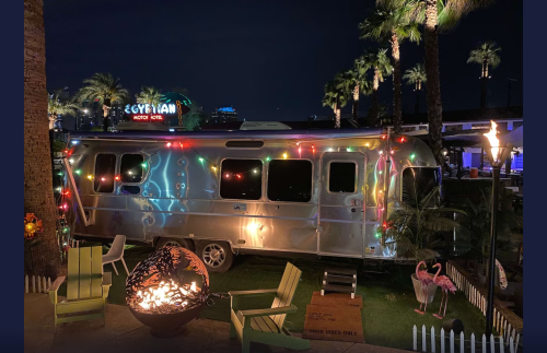 A silver Airstream trailer decorated with colorful lights, surrounded by palm trees at night.