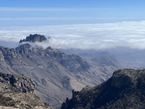 A panoramic view of rugged mountains above a sea of clouds under a clear blue sky.