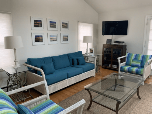 A cozy living room with a blue sofa, striped chairs, a glass coffee table, and framed pictures on the wall.