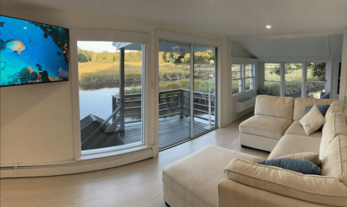 A cozy living room with a large window view of a serene water scene and a TV displaying underwater visuals.