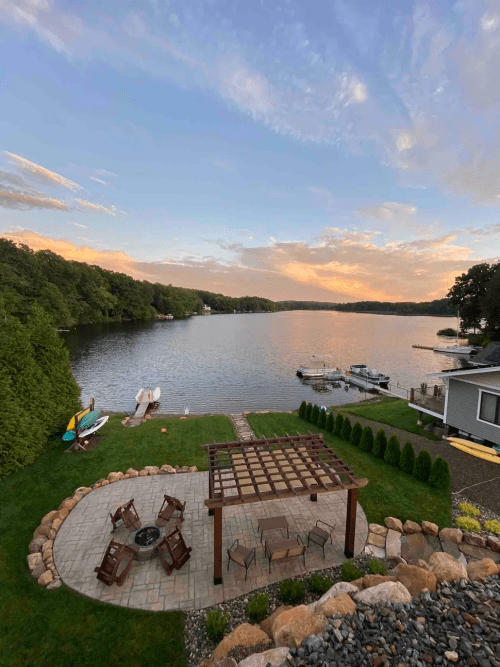 A serene lakeside view at sunset, featuring a patio with a fire pit and boats docked nearby.