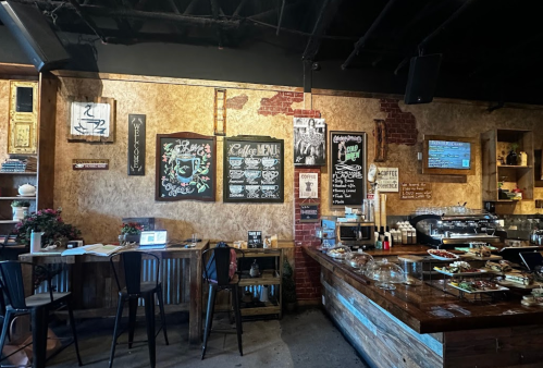 Cozy café interior with a wooden counter, chalkboard menus, and rustic decor. Tables and chairs are set for customers.