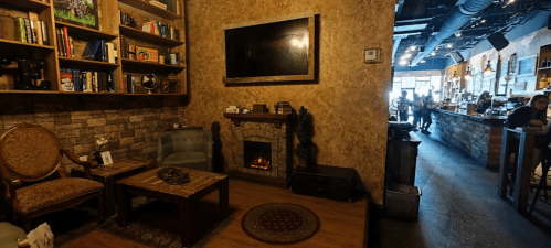 Cozy interior of a café with bookshelves, a fireplace, and a warm atmosphere, featuring seating and a bar area in the background.
