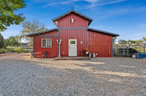 A red barn-style building with a gravel driveway, surrounded by trees and outdoor seating.