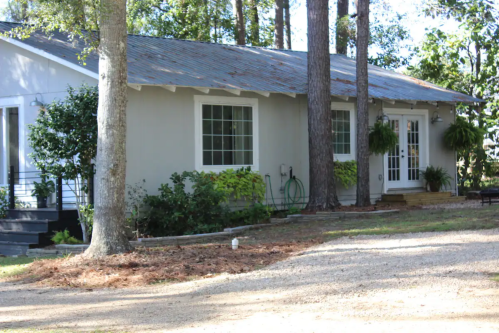 A cozy house surrounded by trees, featuring a front porch and large windows, set in a serene outdoor environment.