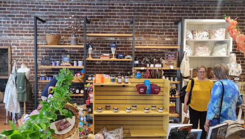 A cozy shop interior with brick walls, shelves of products, and two women browsing among various items.