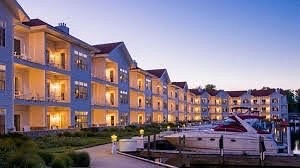 A waterfront hotel with multiple balconies, boats docked nearby, and a serene evening sky.