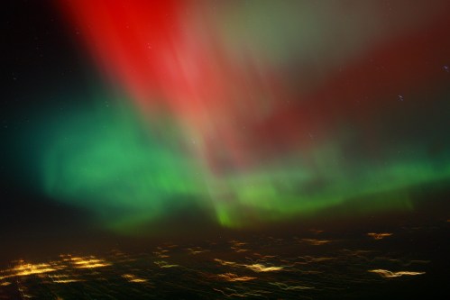 Vibrant auroras in red and green hues illuminate the night sky over a dark landscape.