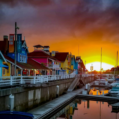 Colorful buildings line a waterfront at sunset, reflecting in calm waters with boats docked nearby.