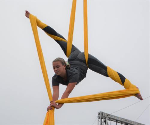 Aerial performer in gray attire gracefully poses on yellow silks, suspended in mid-air with a split position.