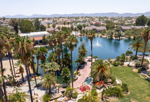 Aerial view of a serene lake surrounded by palm trees and lush greenery, with mountains in the background.