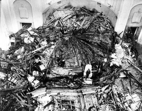 Aerial view of a collapsed building interior, with debris scattered across the floor and structural damage visible.