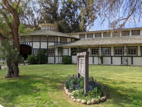 A historic building with a round roof, surrounded by green grass and flowers, under a clear blue sky.