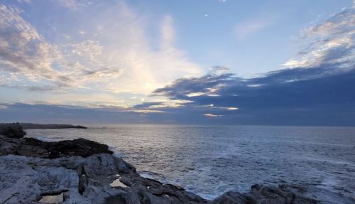 A serene seascape at dusk, featuring rocky shores and a sky filled with soft clouds and gentle hues.