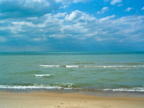 A serene beach scene with gentle waves, sandy shore, and a cloudy blue sky above.