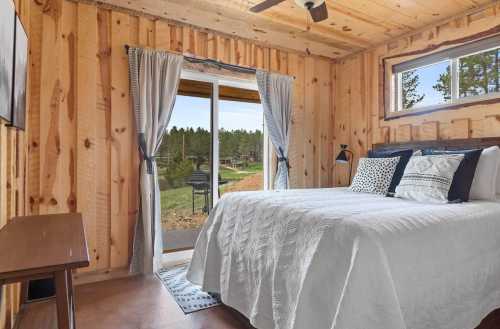 Cozy bedroom with wooden walls, a queen bed, and a view of nature through a sliding glass door.