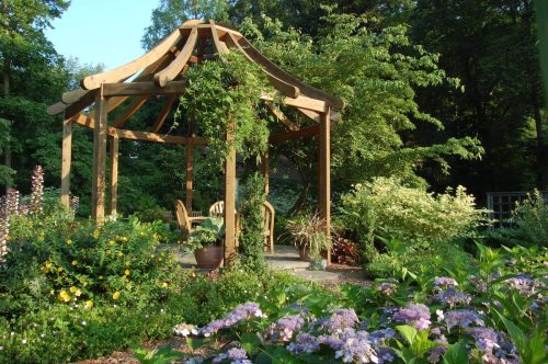 A wooden gazebo surrounded by lush greenery and colorful flowers in a serene garden setting.