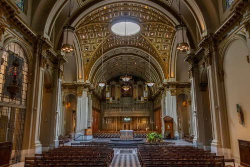 Interior of a grand church featuring a high arched ceiling, ornate details, and rows of wooden pews.