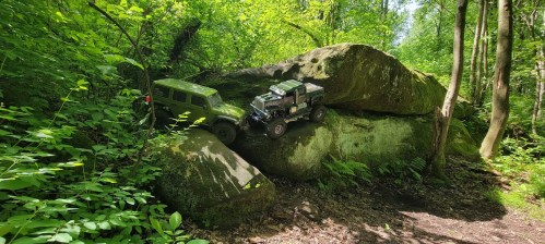 Two toy off-road vehicles are positioned on a large rock in a lush green forest setting.
