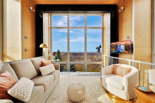 Bright living room with large windows, a cozy sofa, telescope, and scenic outdoor view. Modern decor and warm colors.