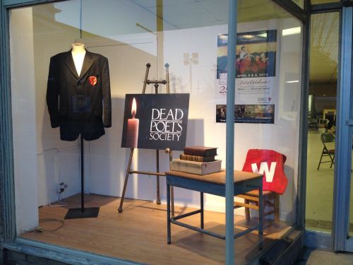 Display window featuring a blazer, books, a candle, and a sign for "Dead Poets Society" with event details.